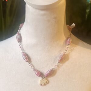 Necklace with shiny orangesicle beads alternating with pink seed beads with a white stone elephant charm on a white body form with a dark background