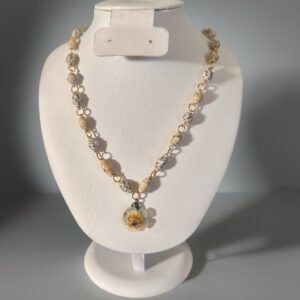 Necklace made of alternating mini yellow-cream and pinstripe on white beads with gold fixings and a white and yellow flower charm on a white form with a neutral background