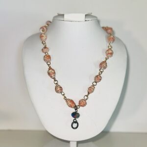 Necklace with orange and white beads on gold fixings with a dark crystal and metal charm on a white form with a neutral gray background