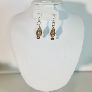 Tan teardrop shaped dangle earrings with gold glitter, gold fixings, copper seed beads on a cream background pile of sand with an ocean background