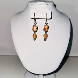 Drop earrings with gold fixings with orange and green cylinder beads and a drop level of orange and white ball beads atop orange seed beads on a neutral background