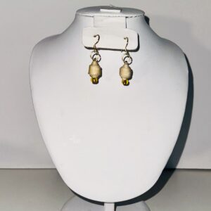 Butter yellow dangle earrings with the shape of mini barrels with gold fixings on a pile of sand with a neutral background