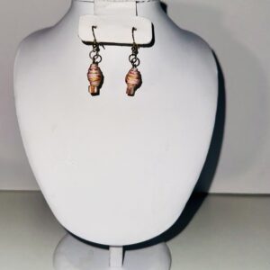 Gold fixings on earrings of pink with fiesta design and colors with glass pink square beads on a pile of sand with the beach and ocean in the background