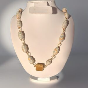 Delicate floral patterned paper beads in a necklace with a glass pendant and silver fixings on a white form with a neutral background