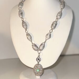 A necklace of silver and white beads covered with silver glitter with silver fixings and a two tiered metal and crystal charm with silver fixings on a white form with a neutral background