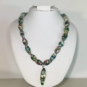 A necklace of paper-based beads from a design of a deconstructed garden with various greens and pinks from flowers, with a large bead charm with a white flower, on a white body form with a neutral background