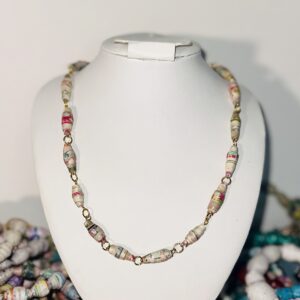 A white necklace form set in the middle of a variety of bracelets and holding a paper bead necklace with colors that tend to red and black and were gel printed by me.