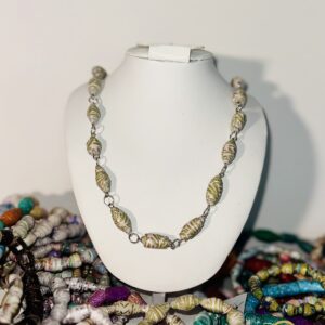 White necklace form set in the midst of a variety of bracelets and displaying a paper bead necklace of green and pink beads.
