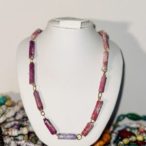 A white necklace form set in the midst of a collection of bracelets displaying a red toned paper bead necklace.