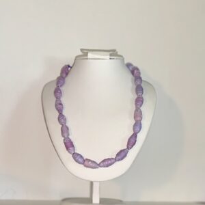 Necklace of lavender beads on a satin cord on a white necklace stand against a neutral background