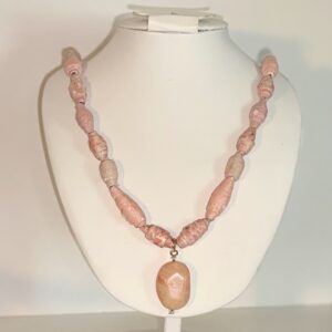 Necklace of coral paper beads with a large glass coral charm on a white form with a neutral room background