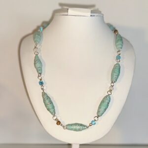 Bright blue paper beads with fancy silver lines, silver fixings and glass beads on a white necklace form against a neutral background
