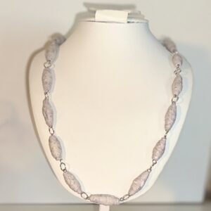 Necklace of white and cream textured pattern paper beads with silver fixings on a white form with a neutral background
