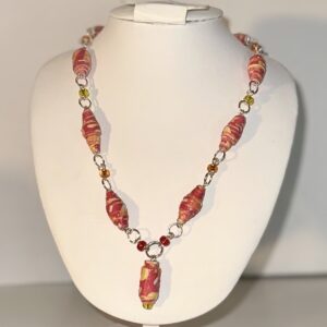 A necklace of fiery red and yellow beads alternating with seed beads of yellow, red and orange, with gold fixings on a white form with a neutral background