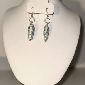 Dangle earrings with silver fixings made of paper-based beads - white with small blue flowers with gold and black, and a single silver seed bead at the base.