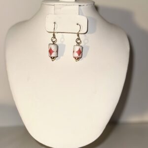 White cylinder earrings with a red diamond shape and a gold ball base with gold fixings on a neutral background
