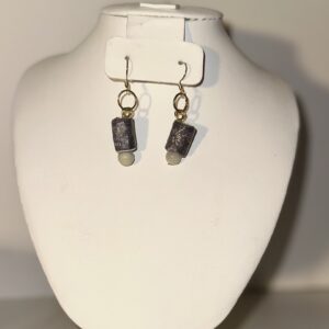 Earrings with black cylinder beads with a small gray bead at the base. Gold fixings and a neutral background.