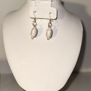 Cream cylinders with tan shapes overlaid earrings with silver fixings on a glass plate on a neutral background