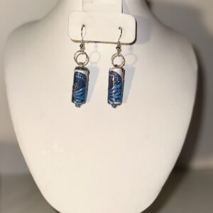 Earrings of long white cylinders with dark blue butterfly image, with silver fixings on a neutral background