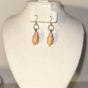 Earrings of yellow and pink beads with gold fixings hanging over a gold tray from a wire against a neutral background