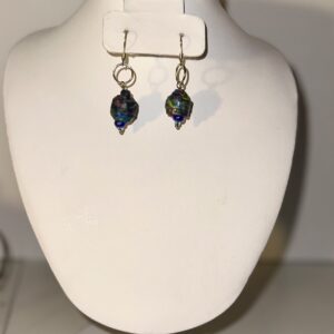 Earrings with gold fixings and black beads with saturated blues, greens and reds on a neutral background