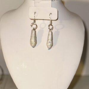 Earrings with silver fixings and beads that are white with tiny blue flowers sporadically spaced on a neutral background